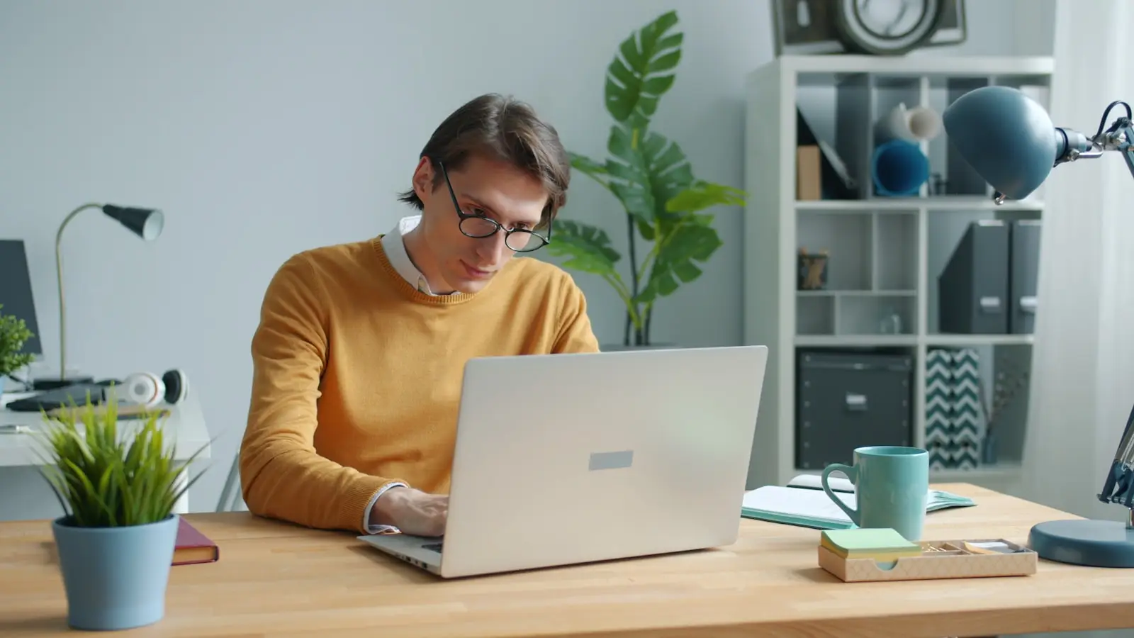 Mitarbeiter in gelbem Pullover arbeitet konzentriert am Laptop im Büro