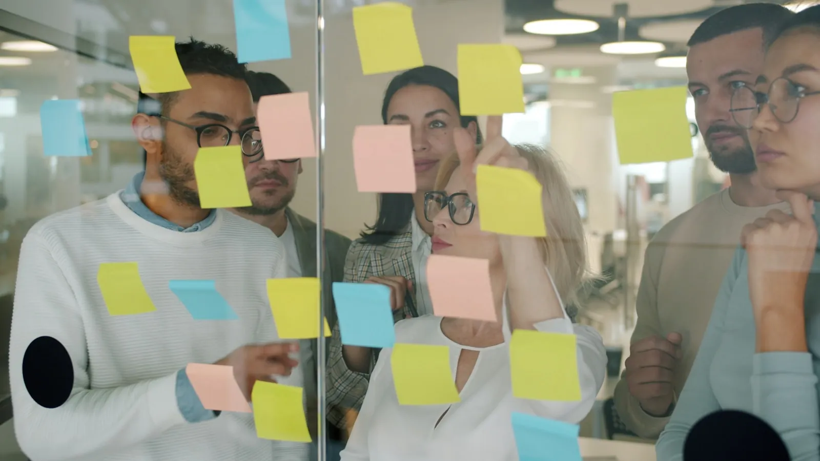 Team plant Aufgaben mit Klebezetteln an einer Glaswand — Microsoft Planner, Project oder Lists richtig wählen